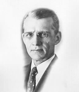 A historical black and white portrait of a man in formal attire and glasses.