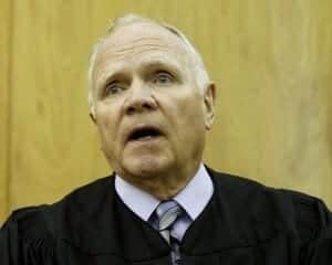 Aging judge speaking in courtroom, judicial robes, legal proceedings, courtroom setting, legal system, courtroom judge, law, justice.