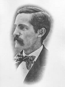 A historic black-and-white portrait of a man with a mustache and bow tie, early 20th-century clothing style.
