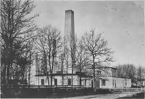 Rustic historic building with tall chimney surrounded by leafless trees, showcasing early industrial architecture.