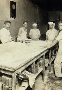 Historic bakery staff preparing bread in early 20th-century bakery kitchen.