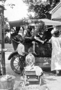Horse-drawn streetcar with passengers and street vendors in front, vintage transportation history.