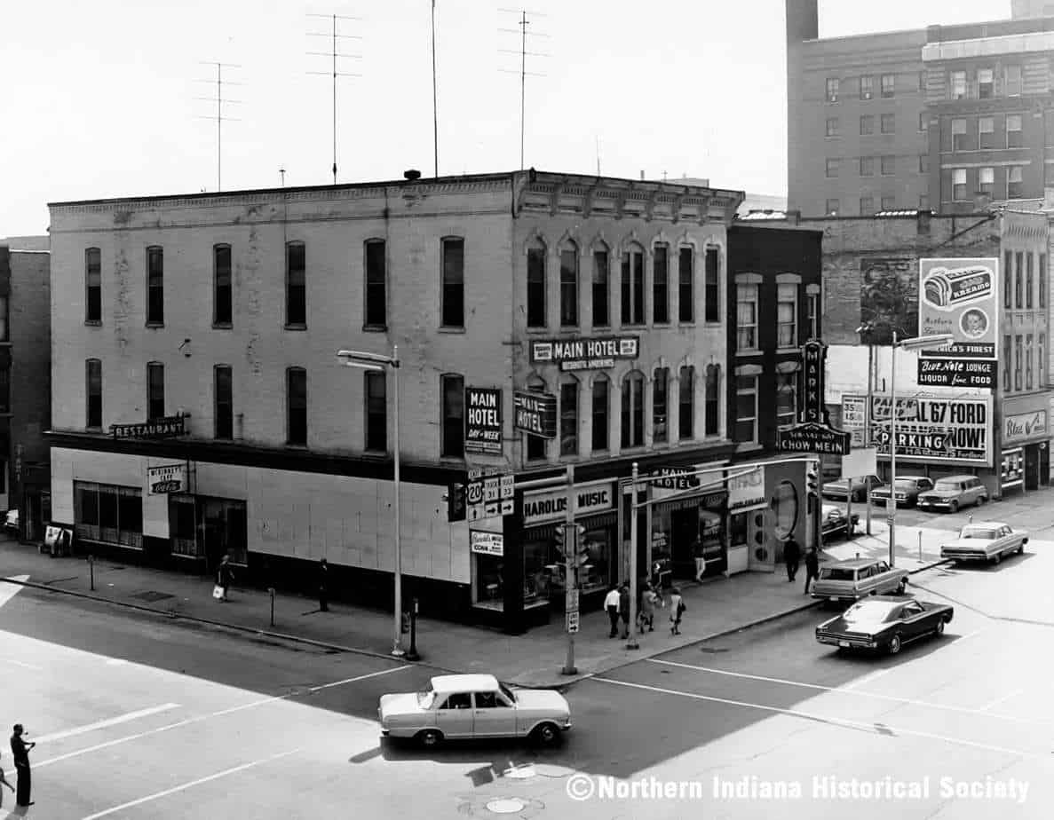 A LOOK BACK - 1960s Main Street ph 1897 Old downtown building with Main Hotel, radio station and storefronts, vintage cars, and pedestrians.
