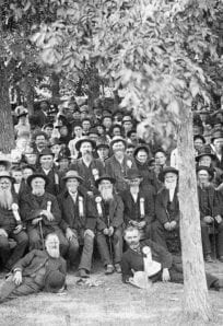 People gathering for a historical event in a park, early 1900s, black and white photograph.