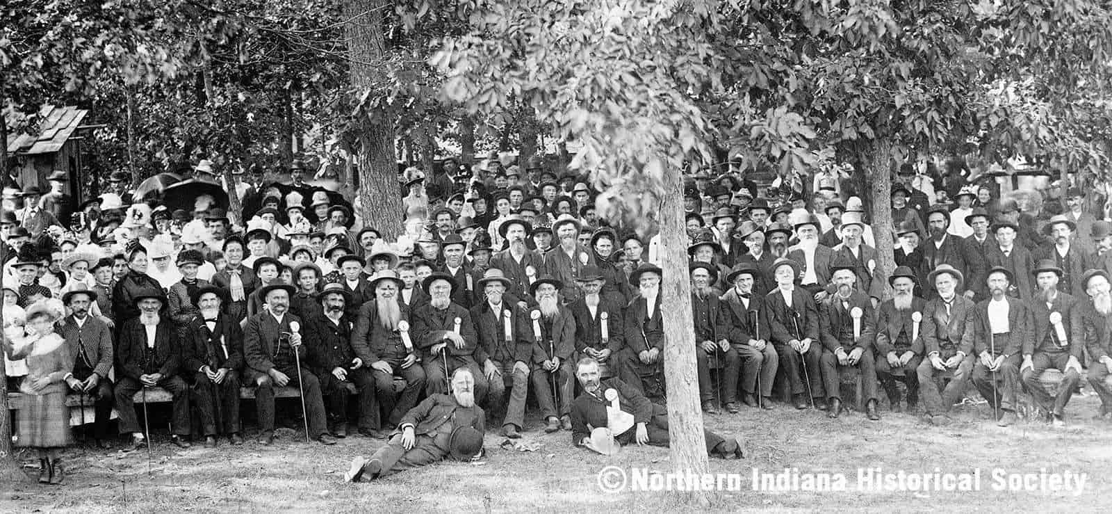 People gathering for a historical event in a park, early 1900s, black and white photograph.