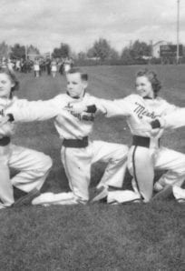 Kids in vintage baseball uniforms performing a formation drill on the field during a game.