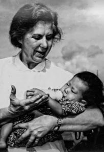 Mother breastfeeding a young child outdoors, historic black and white photo, Navy Pier setting, Second World War era.