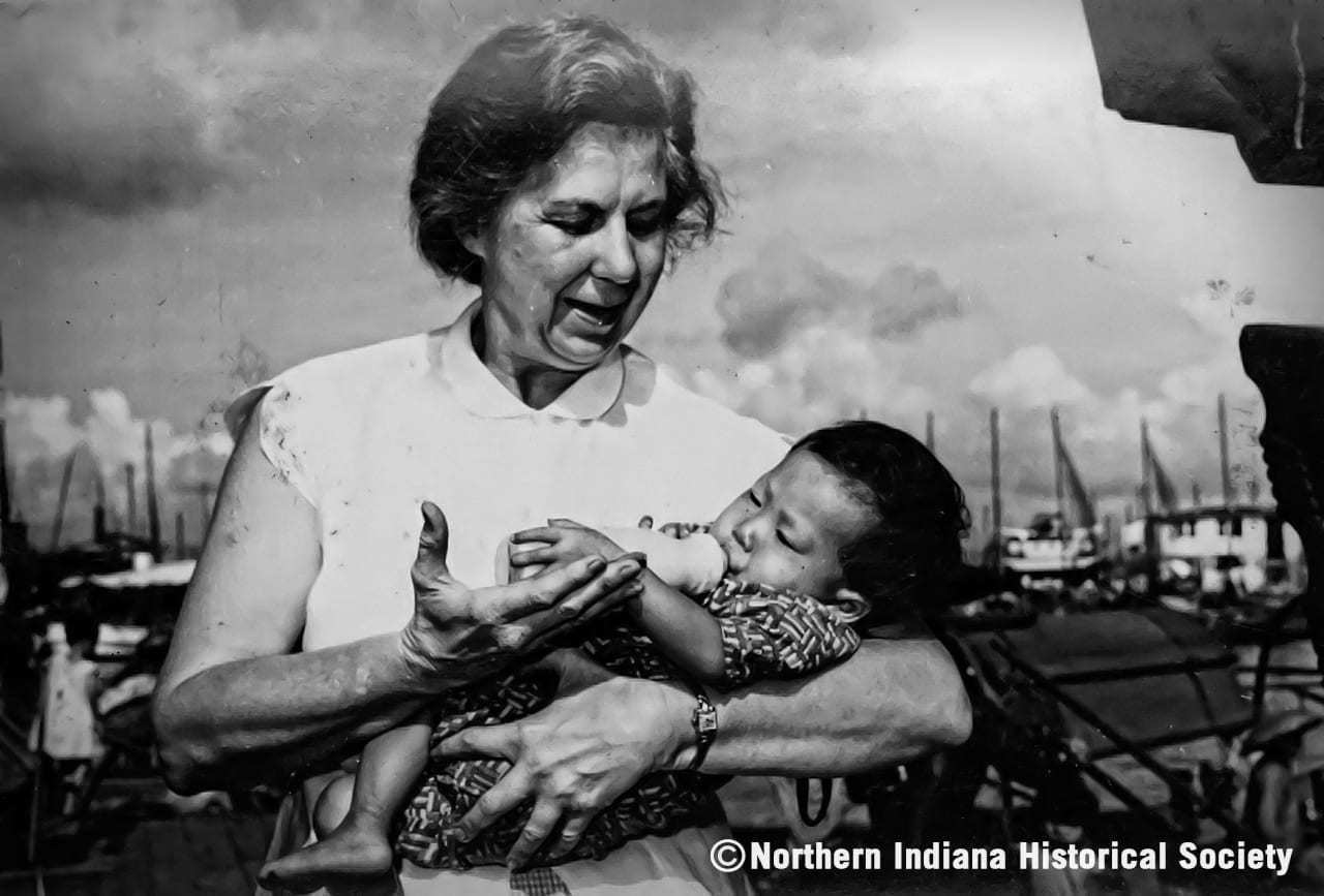 Mother breastfeeding a young child outdoors, historic black and white photo, Navy Pier setting, Second World War era.