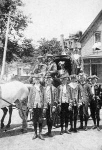 Horse-drawn carriage with people in historic clothing outside a house, vintage photo.