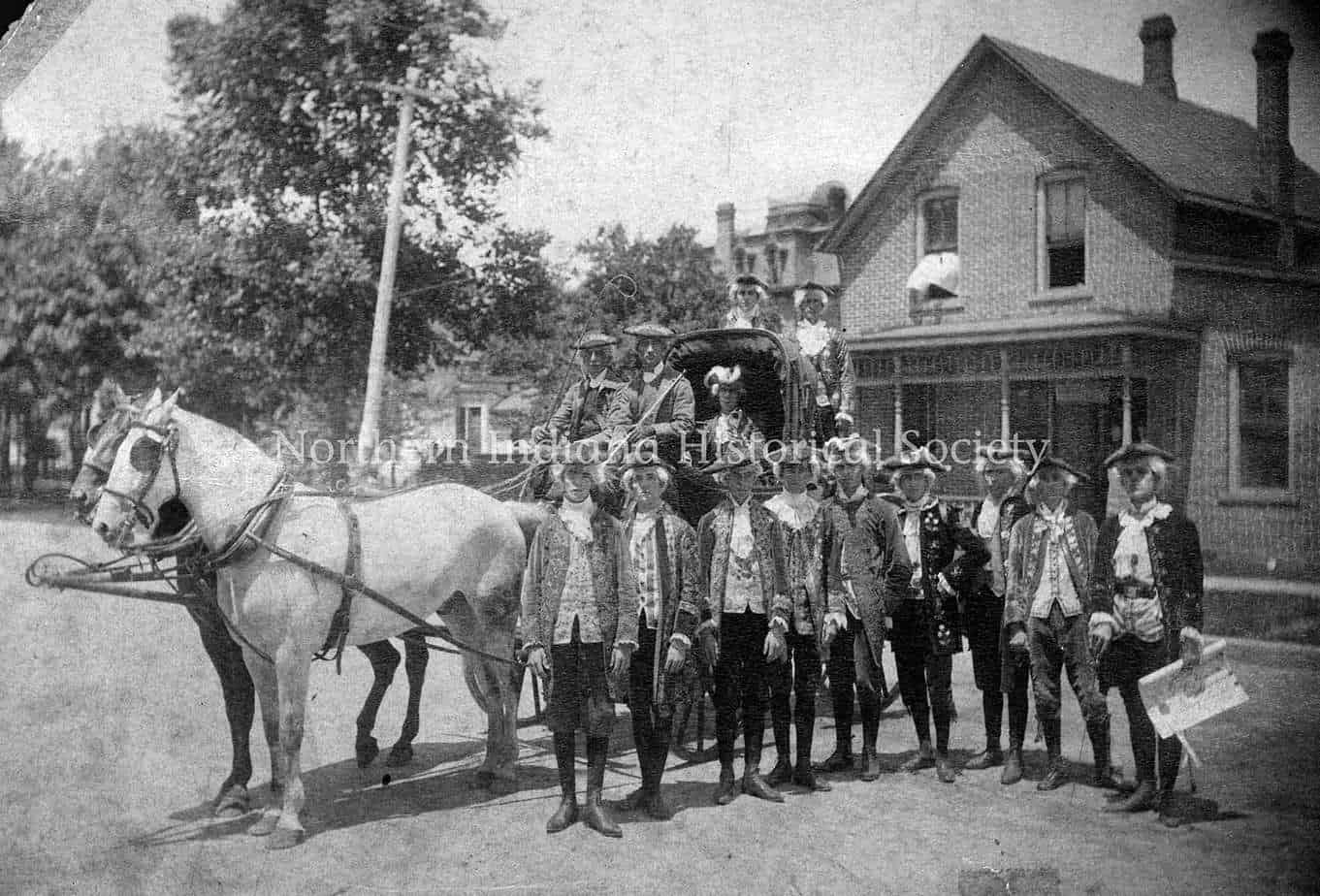 Horse-drawn carriage with costumed children and adults in front of historic house, late 19th century.