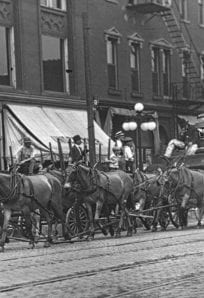 Horse-drawn fire wagon and firefighters in historical downtown Indianapolis, early 20th century.