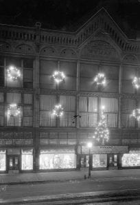 Wyman Department Store decorated with festive holiday lights on a night street scene.