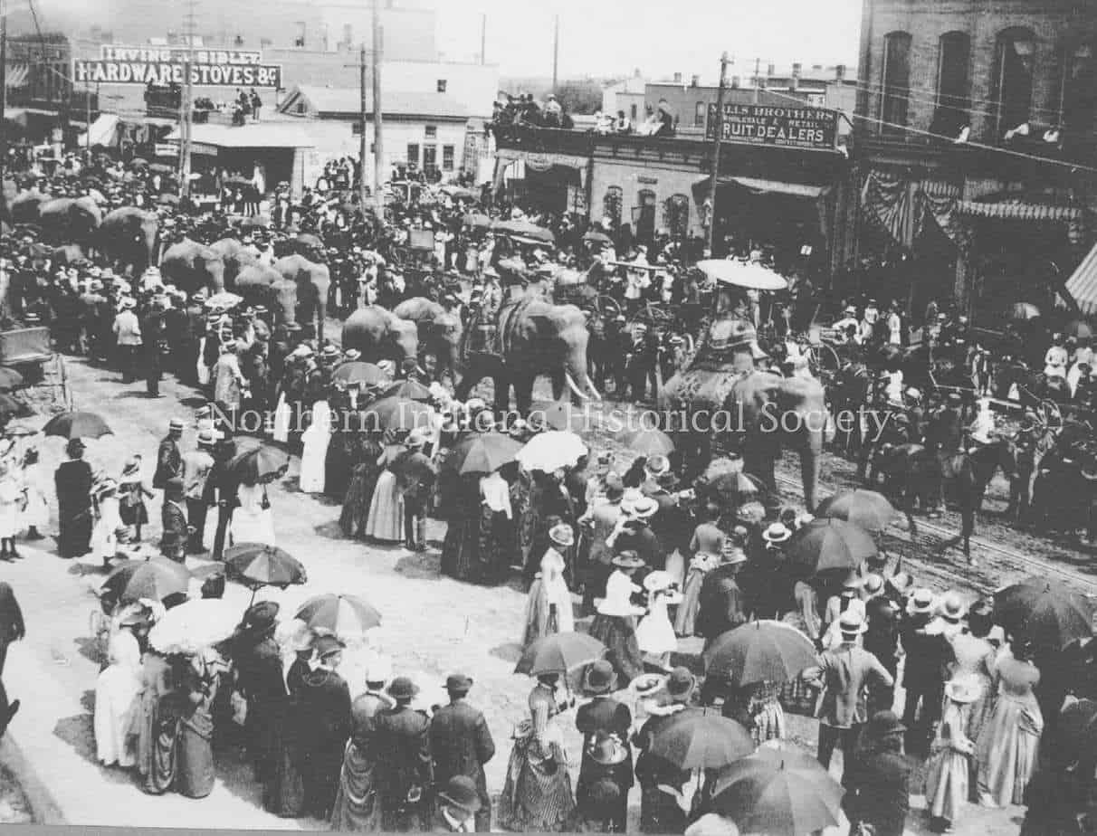 Crowded historical street market scene with horse-drawn carriages and shoppers, early 20th-century urban life in Buffalo, NY.