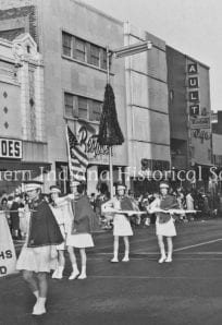 Old black and white parade scene with members of the Emerald Knights marching on city street.