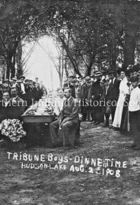 Kids outdoor dinner event in a park, early 1900s, black and white photo, historical school or community gathering.