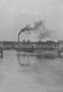 Industrial town with factories and smokestacks along a river in a historic black and white photograph.