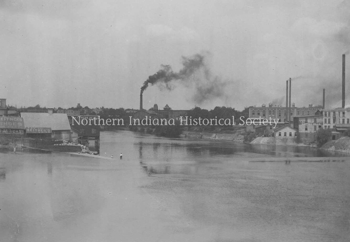 Industrial town with factories and smokestacks along a river in a historic black and white photograph.