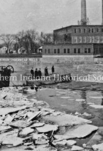 Black and white historical photo of Stevenson Underwear Mills building and workers by a frozen river.