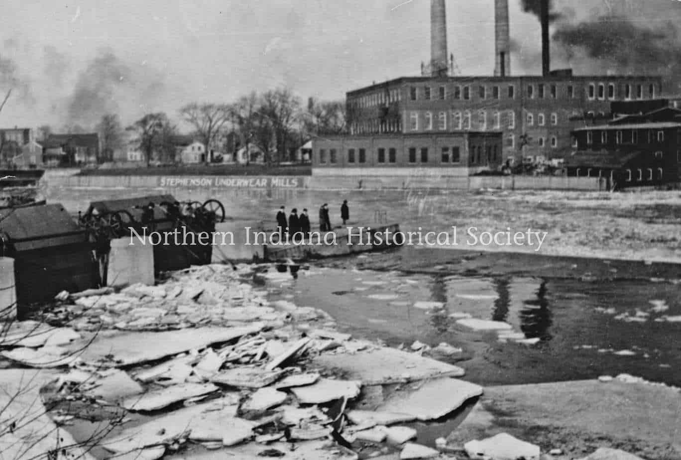 Black and white historical photo of Stevenson Underwear Mills building and workers by a frozen river.