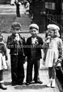 Children eating ice cream in front of a fence, vintage black and white photo.