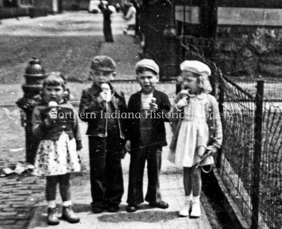 Children eating ice cream in front of a fence, vintage black and white photo.