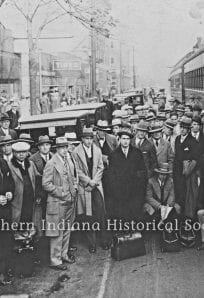 Group of people waiting at a train station in early 20th century, historical transportation scene.