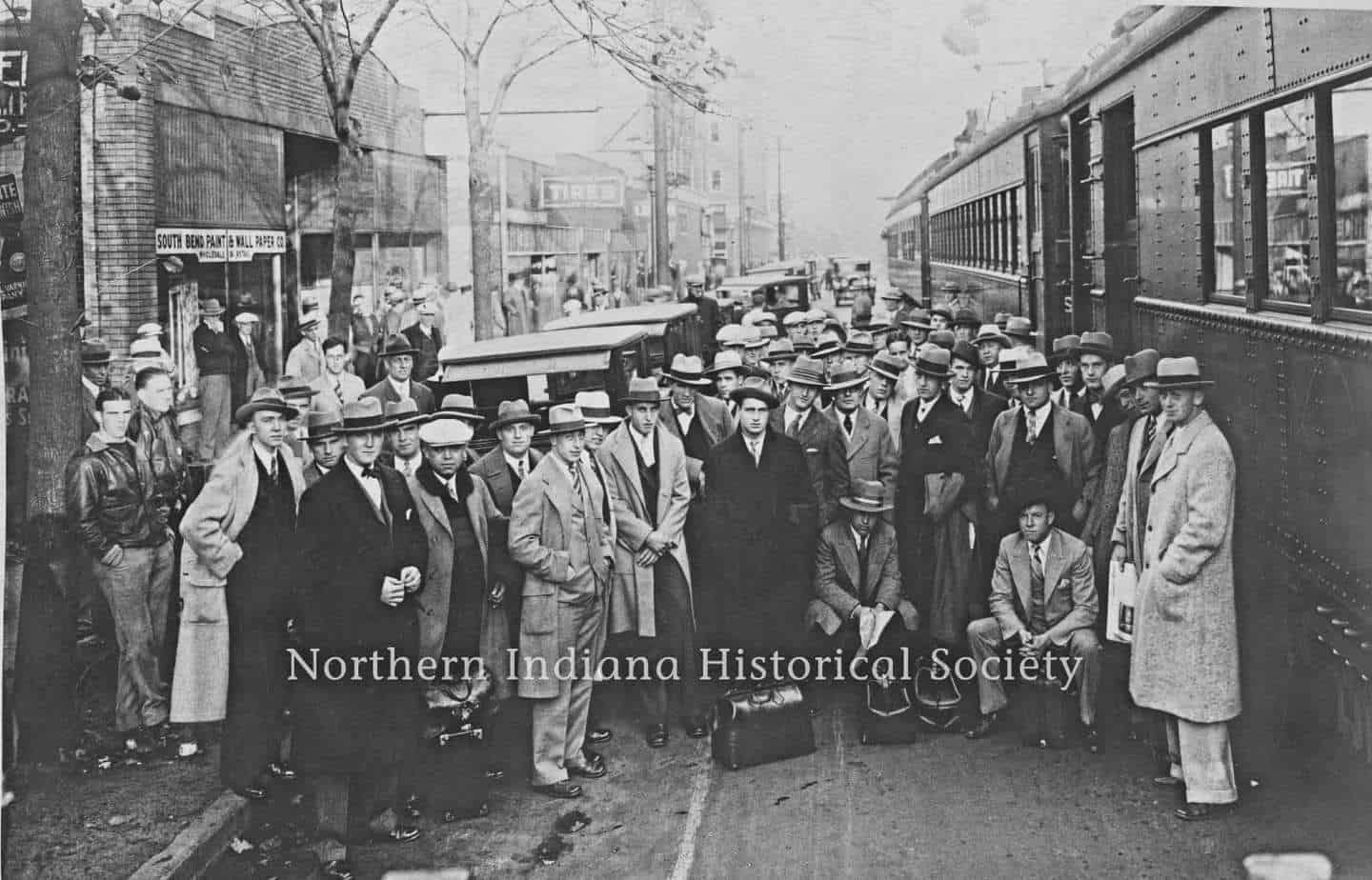 Group of people waiting at a train station in early 20th century, historical transportation scene.
