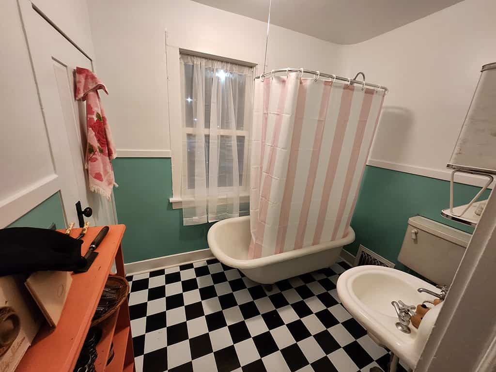 Vintage bathroom with clawfoot tub, pink-striped shower curtain, black and white checkered floor, and retro fixtures.
