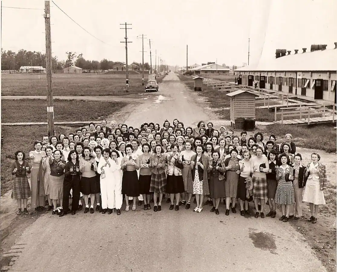 kingsburyplantworkers_LaPorte County Historical Society Museum Women gathered in groups on a dirt road in front of historic buildings, celebrating community and history. This black-and-white photo showcases mid-20th-century rural life and women's social activism at The History Museum.